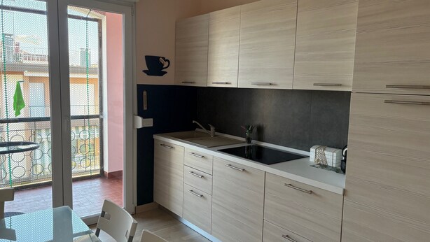 Cocina moderna con armarios de madera clara, encimera negra y puerta de vidrio que da a un balcón.