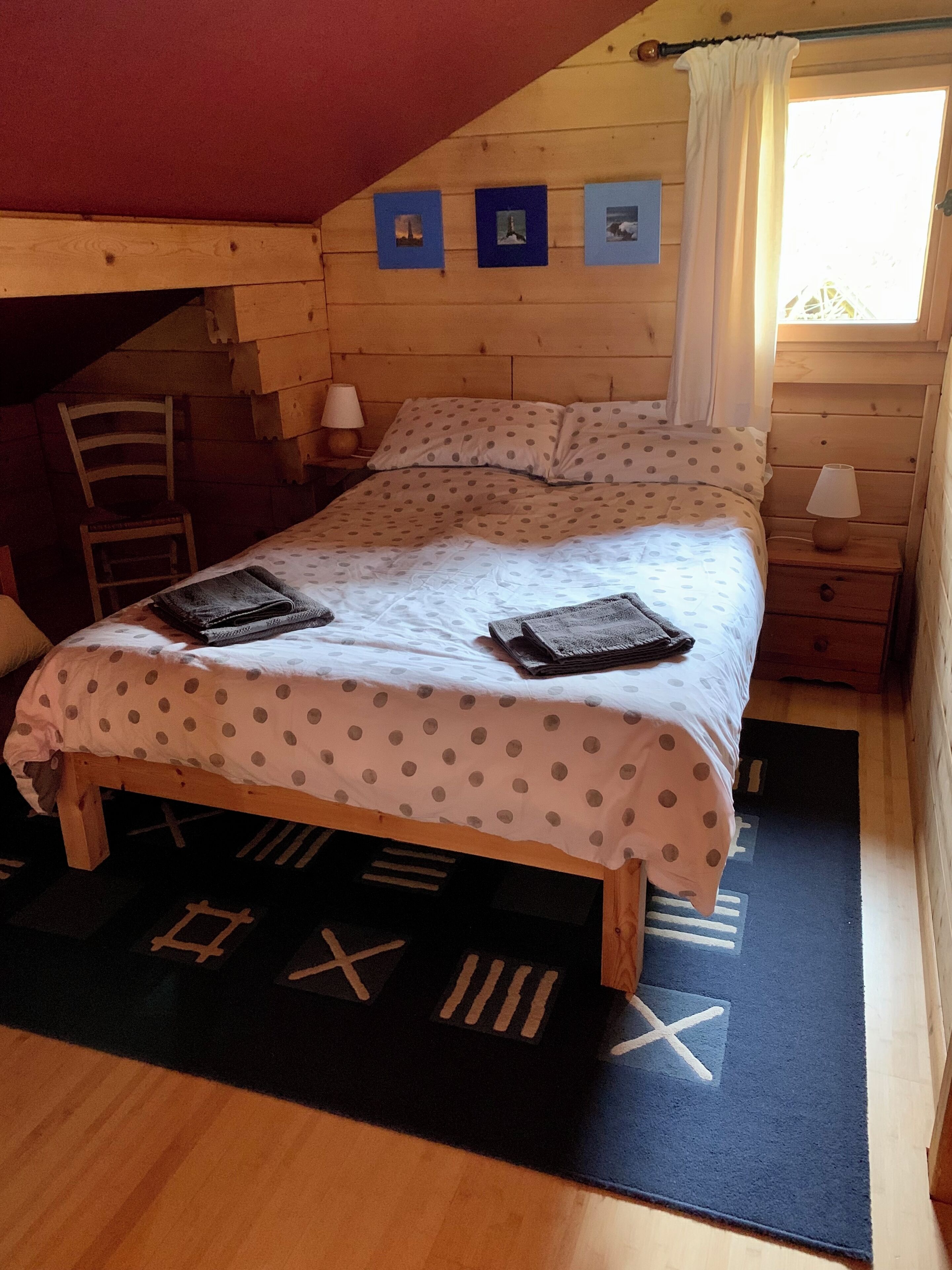 A cozy bedroom with a bed, a chair, a nightstand, and a window with curtains.