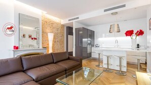 A modern living room with a brown leather sofa, a glass coffee table, and a kitchen area featuring a white countertop, stainless steel appliances, and red flowers. - Exceptional 2-bedroom apartment 74m2 Place Bellecour (Downtown) (Lyon)