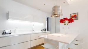 A modern kitchen with white cabinetry, a central island with bar stools, a pendant light, and a vase with red flowers on the wall. - Exceptional 2-bedroom apartment 74m2 Place Bellecour (Downtown) (Lyon)