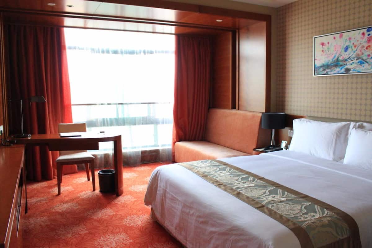 A hotel room with a large bed, a desk, a chair, and a view of the outside.