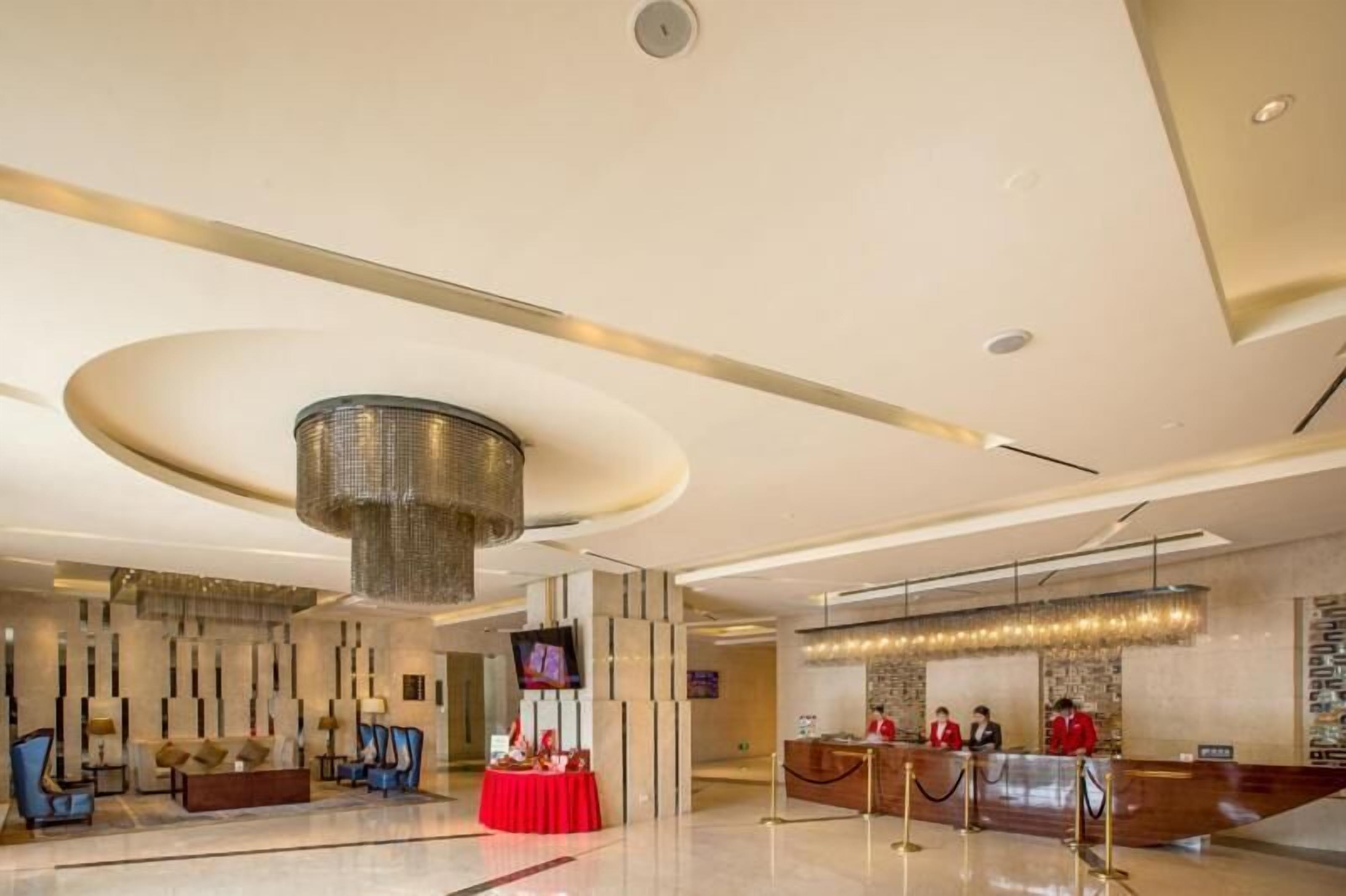 Un hall d’hôtel moderne avec un comptoir d’accueil, un espace salon et un grand lustre.