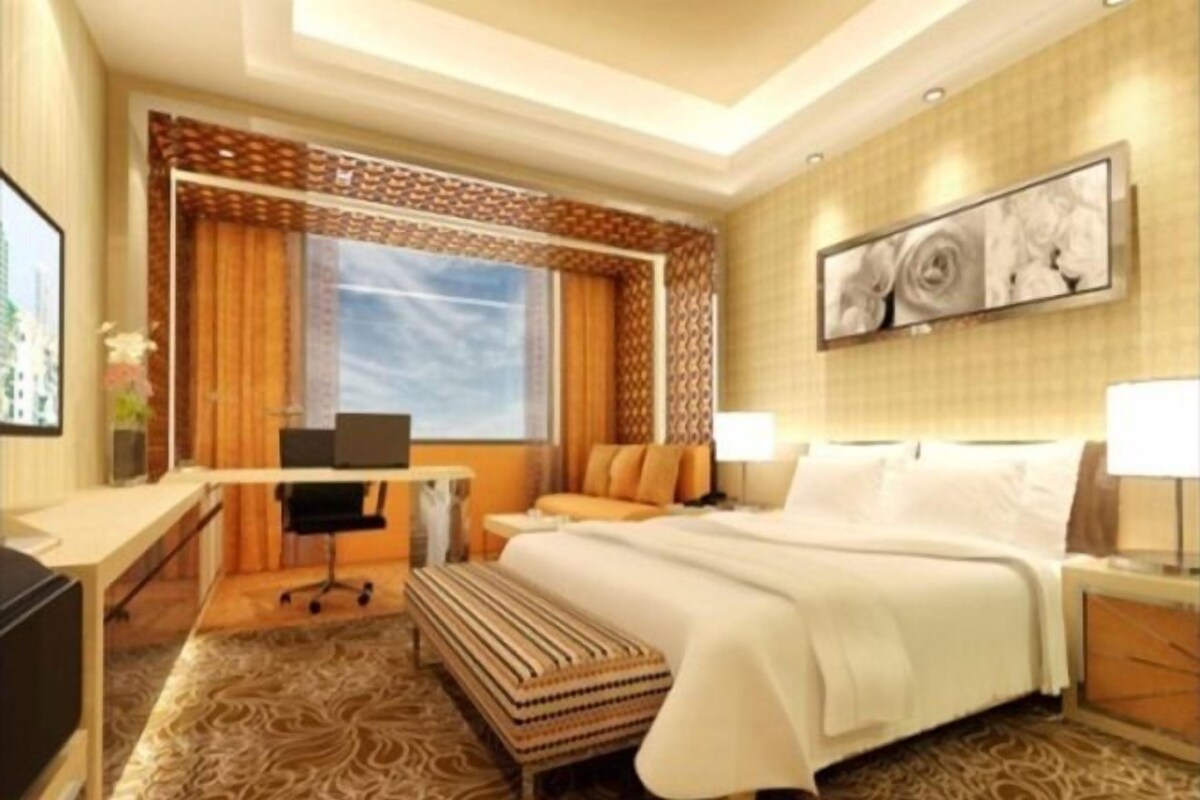 A hotel room with a bed, desk, chair, and a large window with curtains.