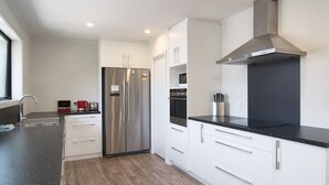 A modern kitchen with stainless steel appliances, white cabinetry, and a black countertop. - Brookside Villa (Christchurch)