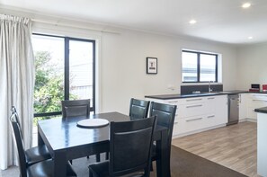 A modern kitchen with a dining area, large windows, and a view of the outdoors. - Brookside Villa (Christchurch)