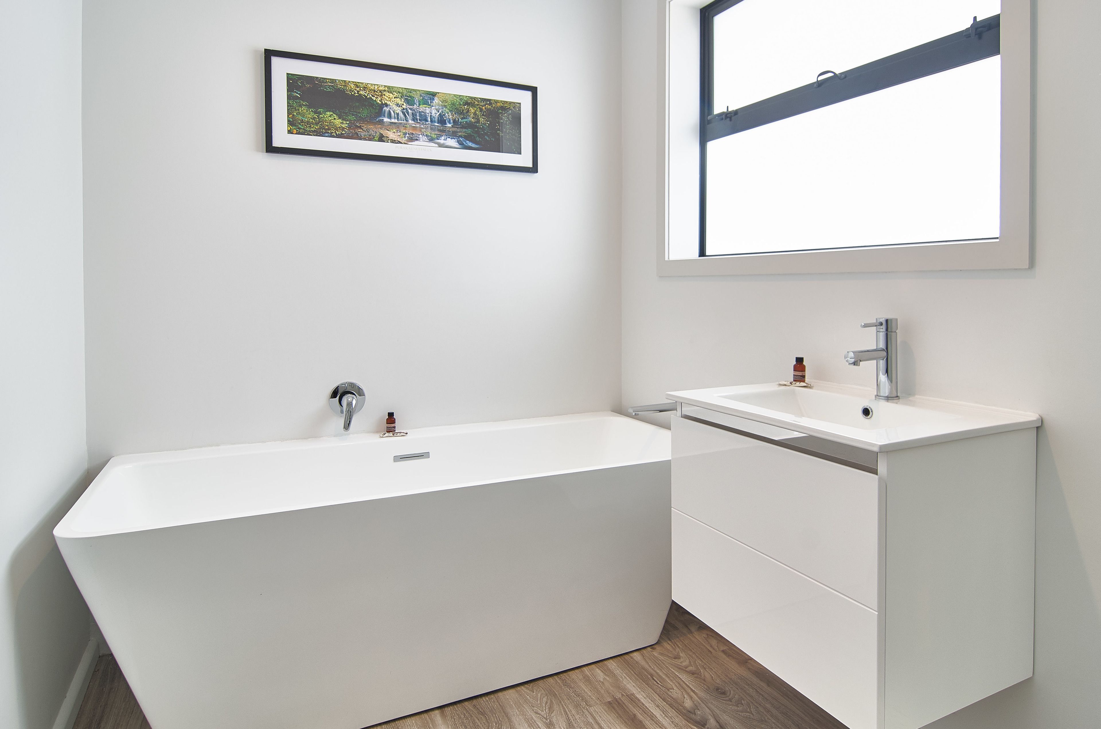 A modern bathroom with a freestanding bathtub, a white sink, and a framed picture on the wall.