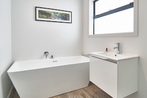 A modern bathroom with a freestanding bathtub, a white sink, and a framed picture on the wall. - Brookside Villa (Christchurch)