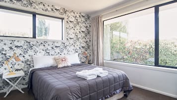 A bedroom with a large bed, floral wallpaper, and a view of greenery through a window.