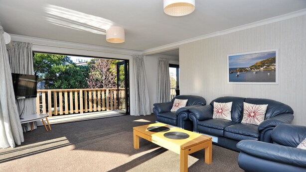 A living room with a sofa set, a coffee table, a TV, and a view of the outdoors. - Brookside Villa (Christchurch)