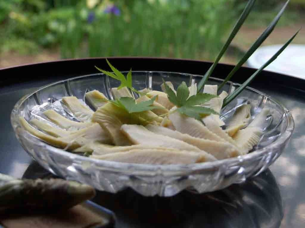 A clear glass bowl containing sliced white fish garnished with green herbs, placed on a reflective surface.