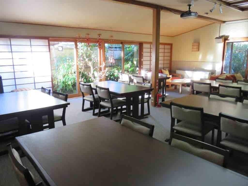 A spacious dining area with multiple tables and chairs, large windows with a view of greenery, and traditional sliding doors.