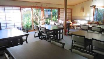 A spacious dining area with multiple tables and chairs, large windows with a view of greenery, and traditional sliding doors.