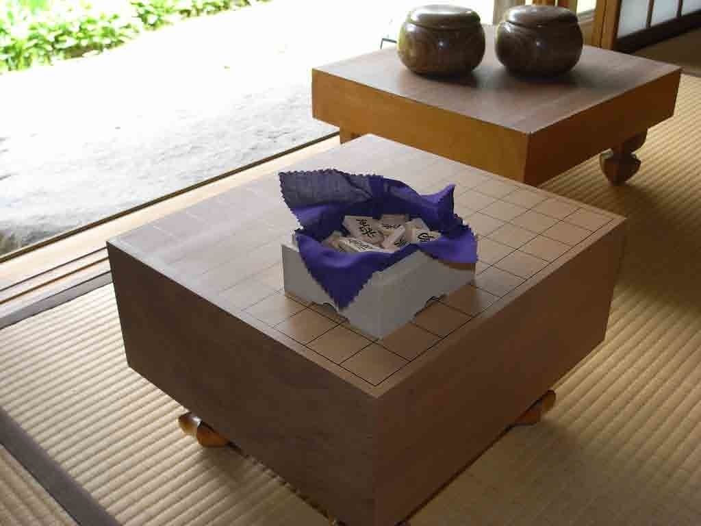 Una habitación japonesa tradicional con suelo de tatami, una mesa de madera baja con un paño azul y una pequeña caja blanca con un paño azul encima.