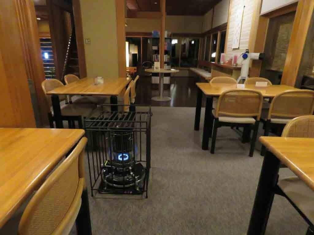 Un restaurante con mesas y sillas de madera, una máquina de café central y vista a la calle.