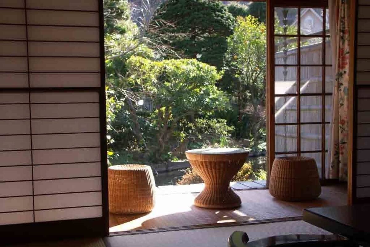 Ein traditioneller japanischer Raum mit Tatami-Böden, einem niedrigen Tisch und Blick auf einen Garten mit Teich und Bäumen.