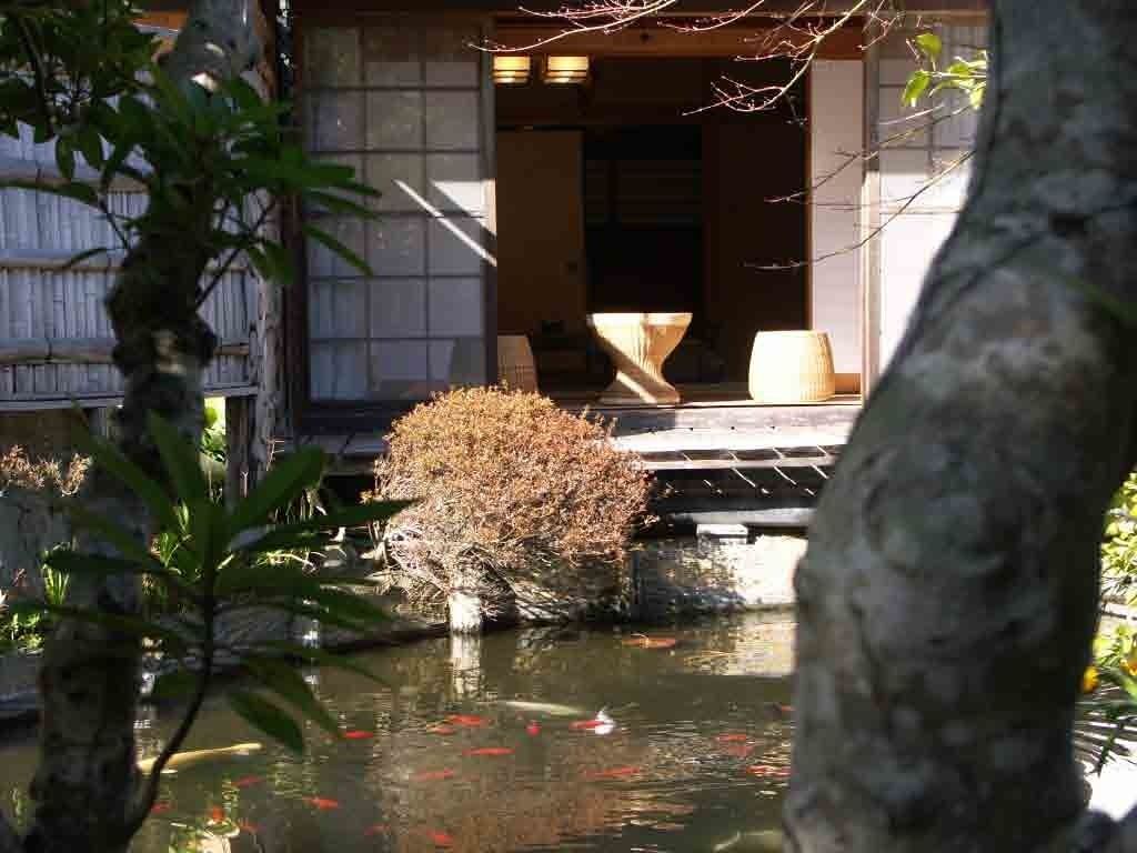 Un jardín japonés tradicional con un estanque de carpas koi, un farol de piedra y un edificio de madera al fondo.