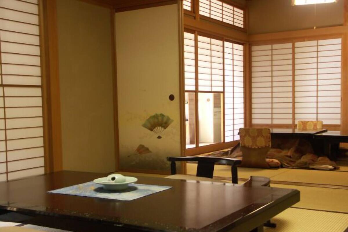 Ein traditioneller japanischer Raum mit Tatami-Böden, einem niedrigen Tisch und einem Fächer sowie verschiebbaren Türen.
