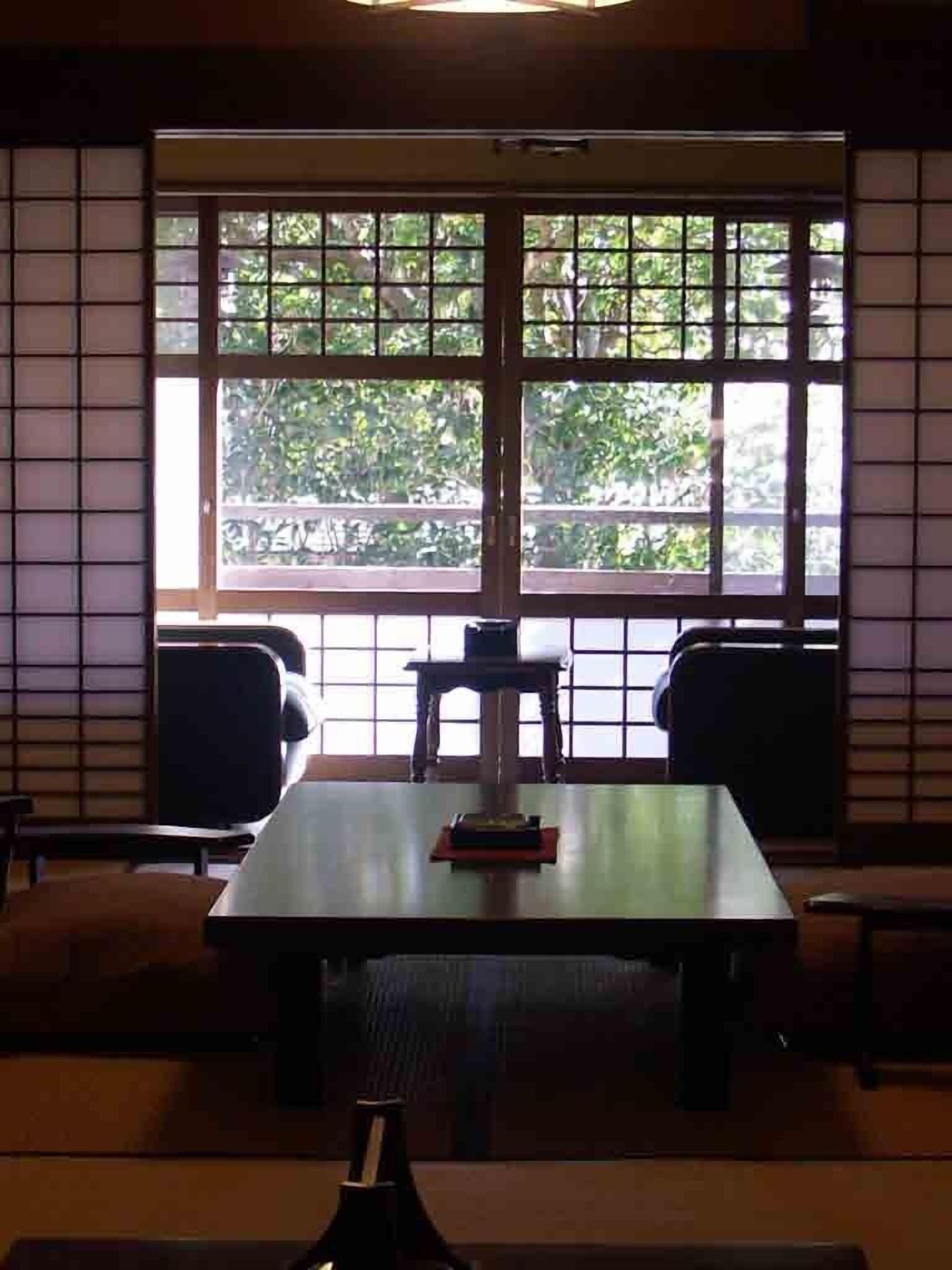 Une salle de conférence avec une grande table, deux chaises et une vue sur l’extérieur à travers une fenêtre à carreaux.