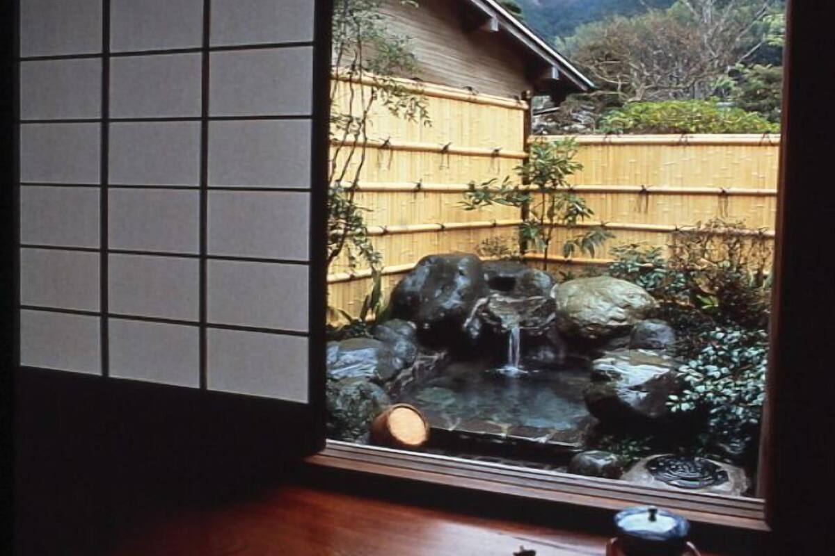 Ein Blick auf einen traditionellen japanischen Garten mit einem kleinen Wasserfall, einem Bambuszaun und einem Holztisch mit Teekanne.