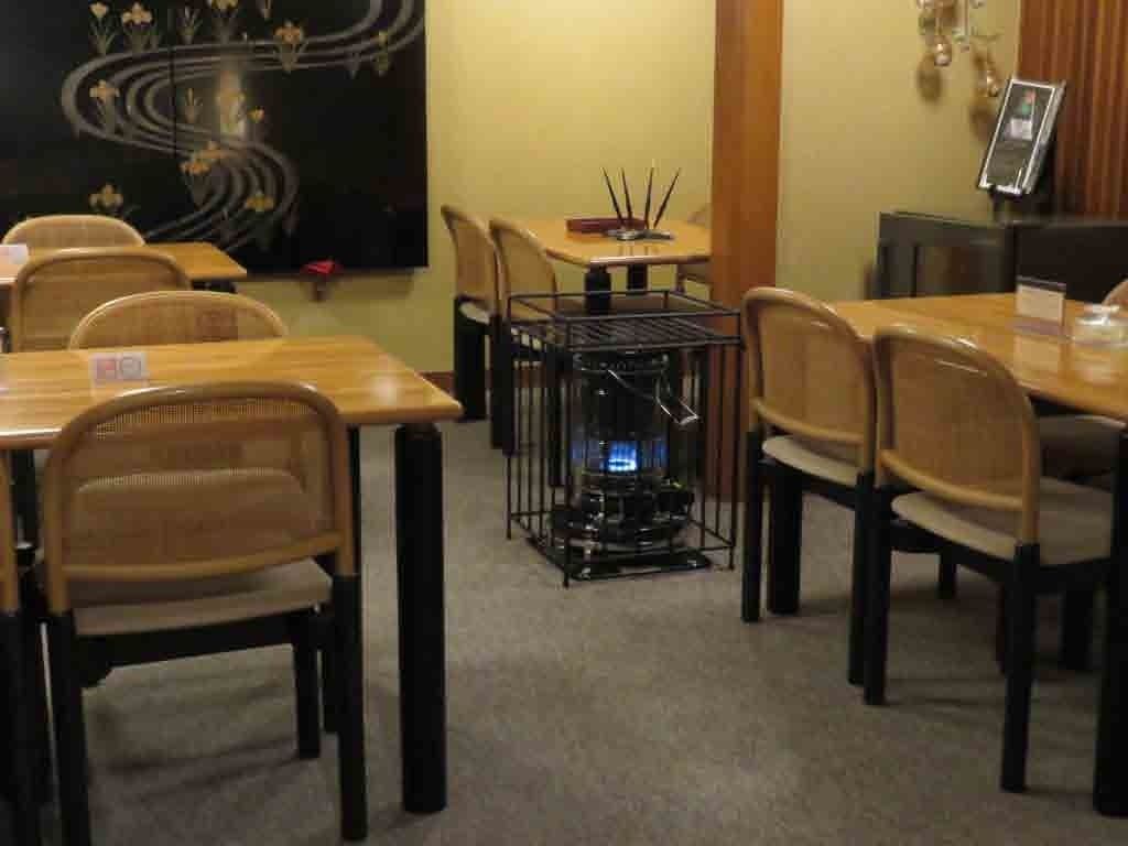 Un espace repas avec des tables et des chaises en bois, un radiateur noir placé au centre et un mur décoratif orné d’un motif floral.