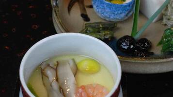 A bowl of soup with various ingredients, a small bowl of sauce, and some vegetables on a table.