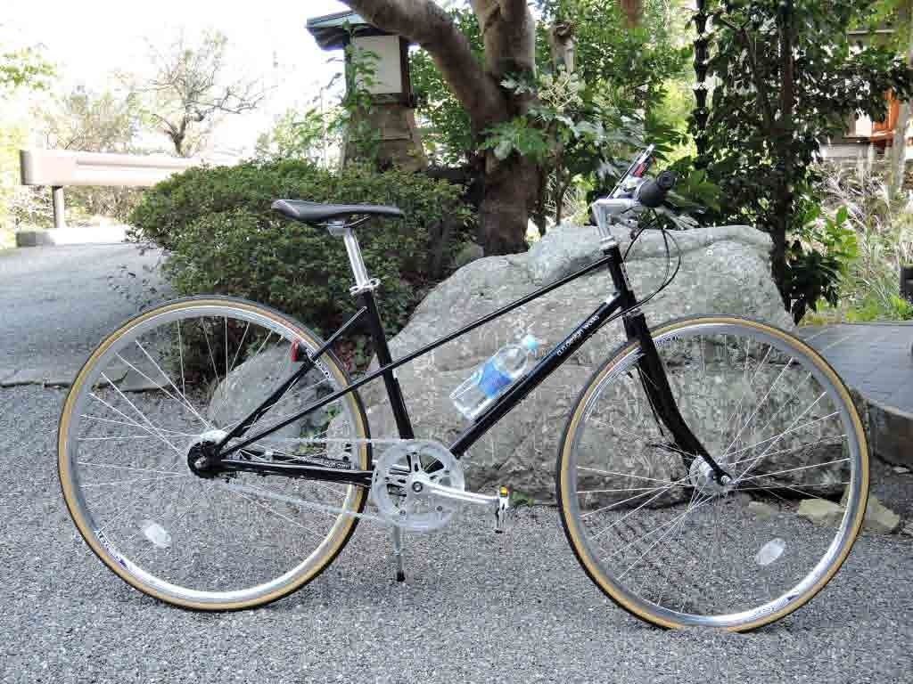 Un vélo est garé sur une surface pavée, avec une structure en pierre et de la verdure en arrière-plan.