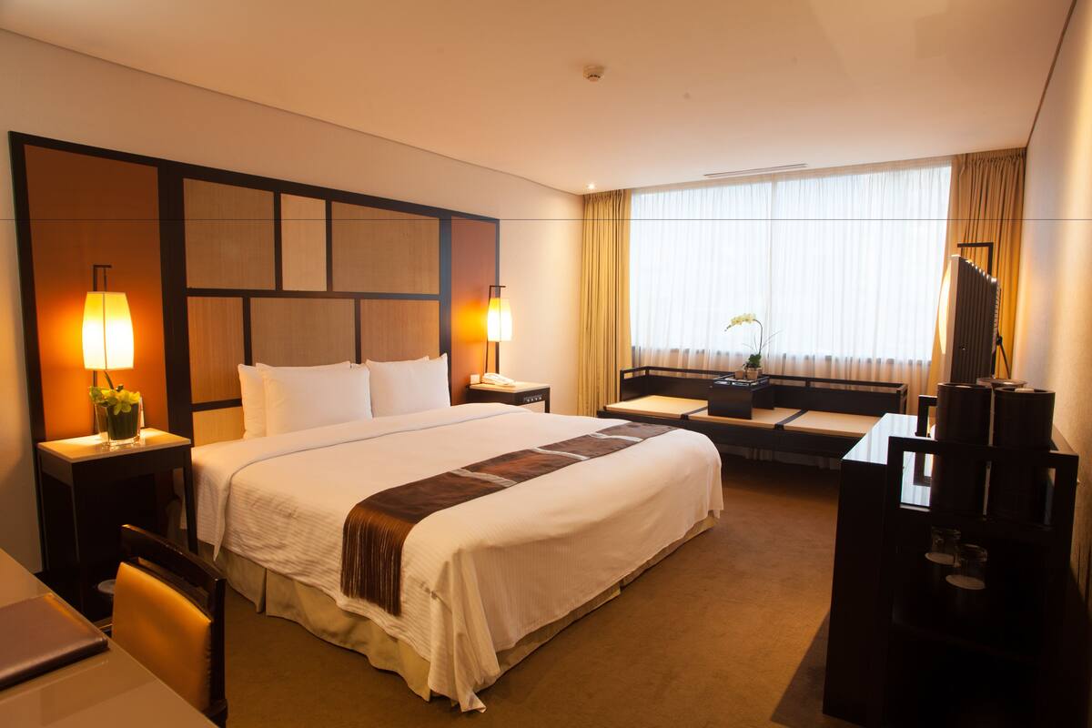 A hotel room with a large bed, bedside tables with lamps, a desk, and a TV.