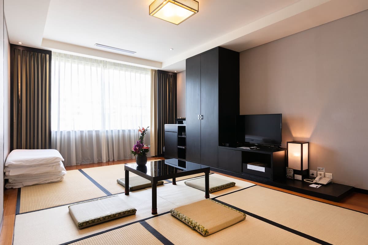 A modern hotel room with tatami mats, a flat-screen TV, a desk, and a sofa.