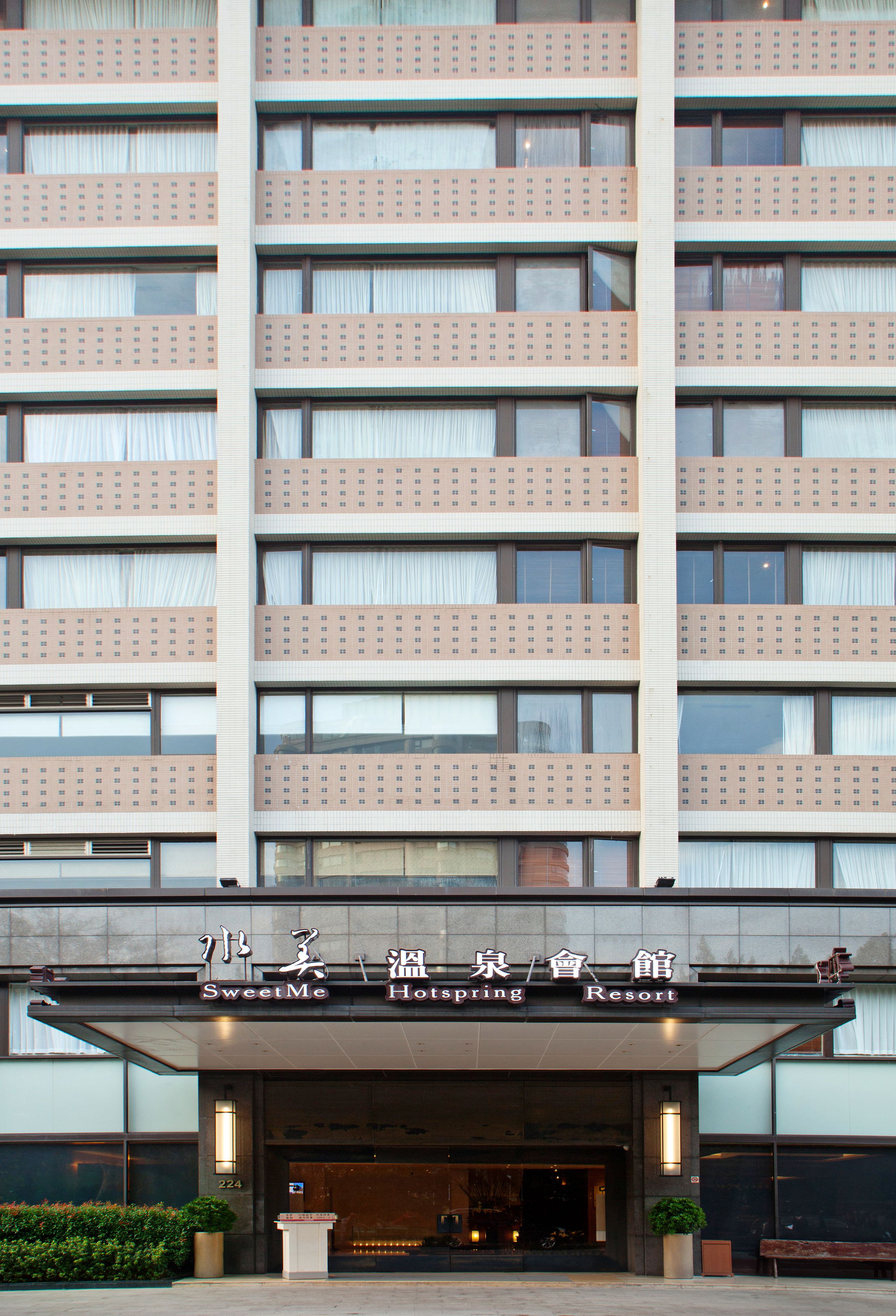 A hotel with a modern facade, multiple balconies, and a sign indicating it is a SweetMe HotSpring Resort.