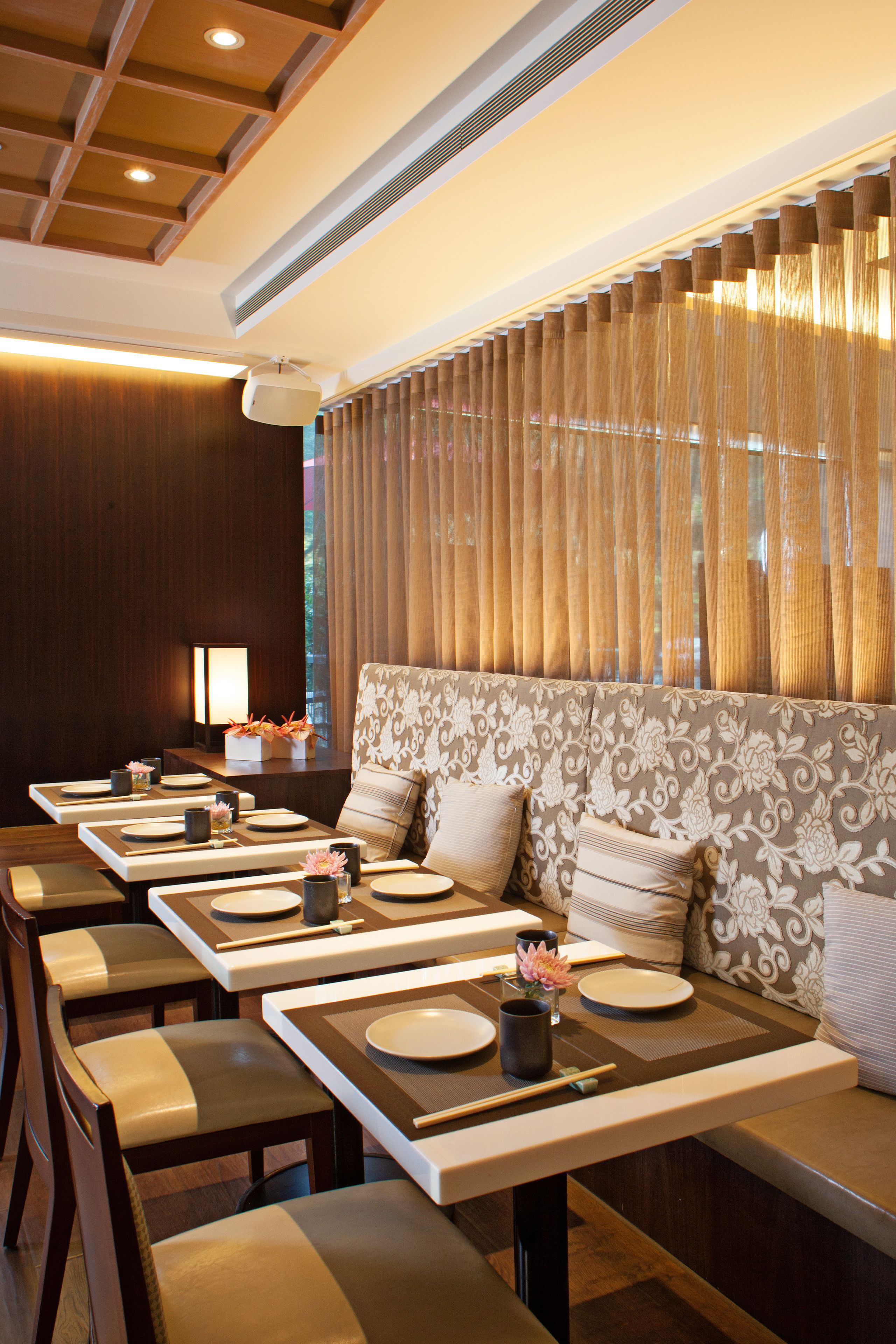 A restaurant with a long communal table, cushioned seating, and a patterned wall.