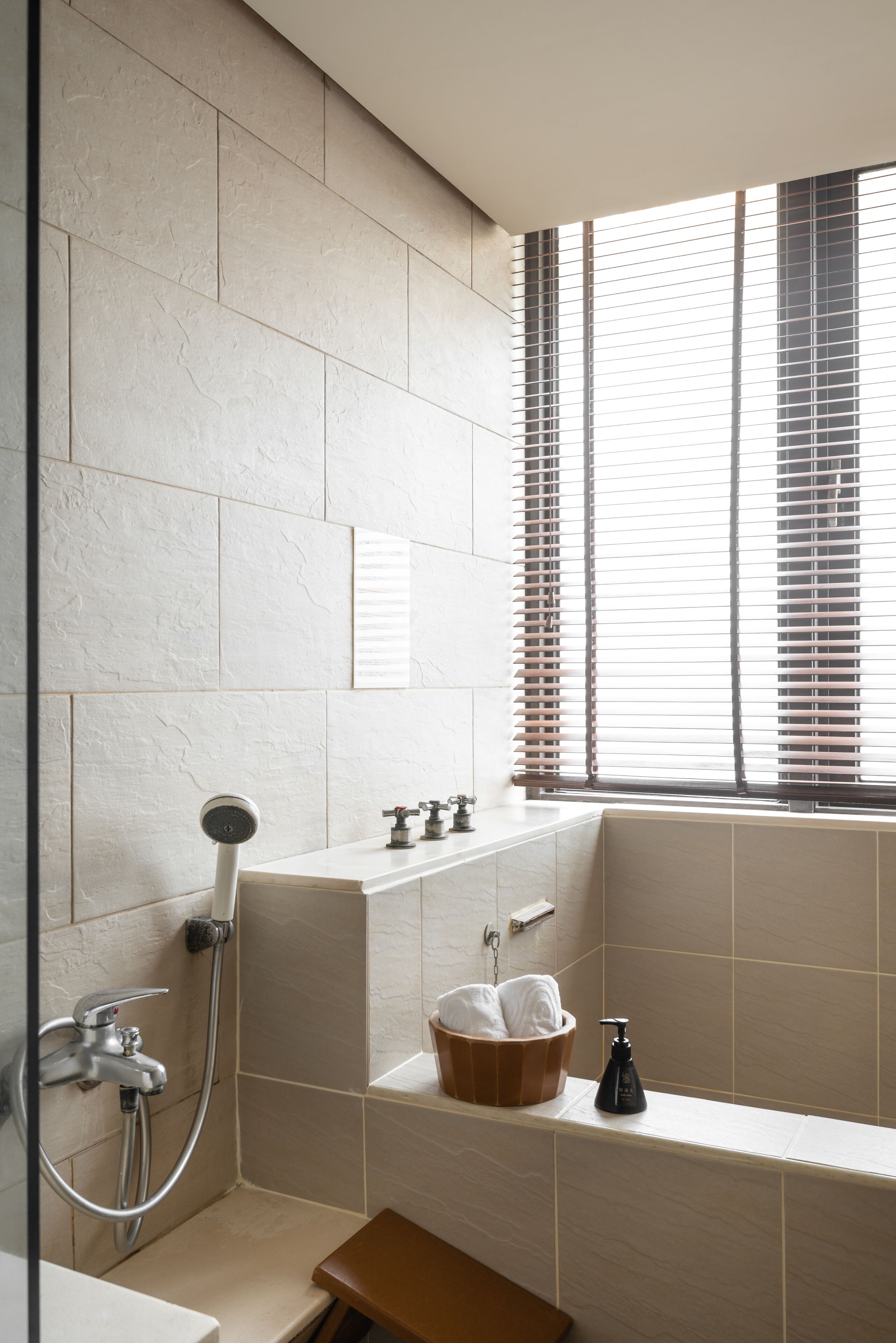 A bathroom with a bathtub, a shower, and a window with blinds.