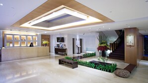 Een moderne hotel lobby met een receptiebalie, een zithoek en een trap.