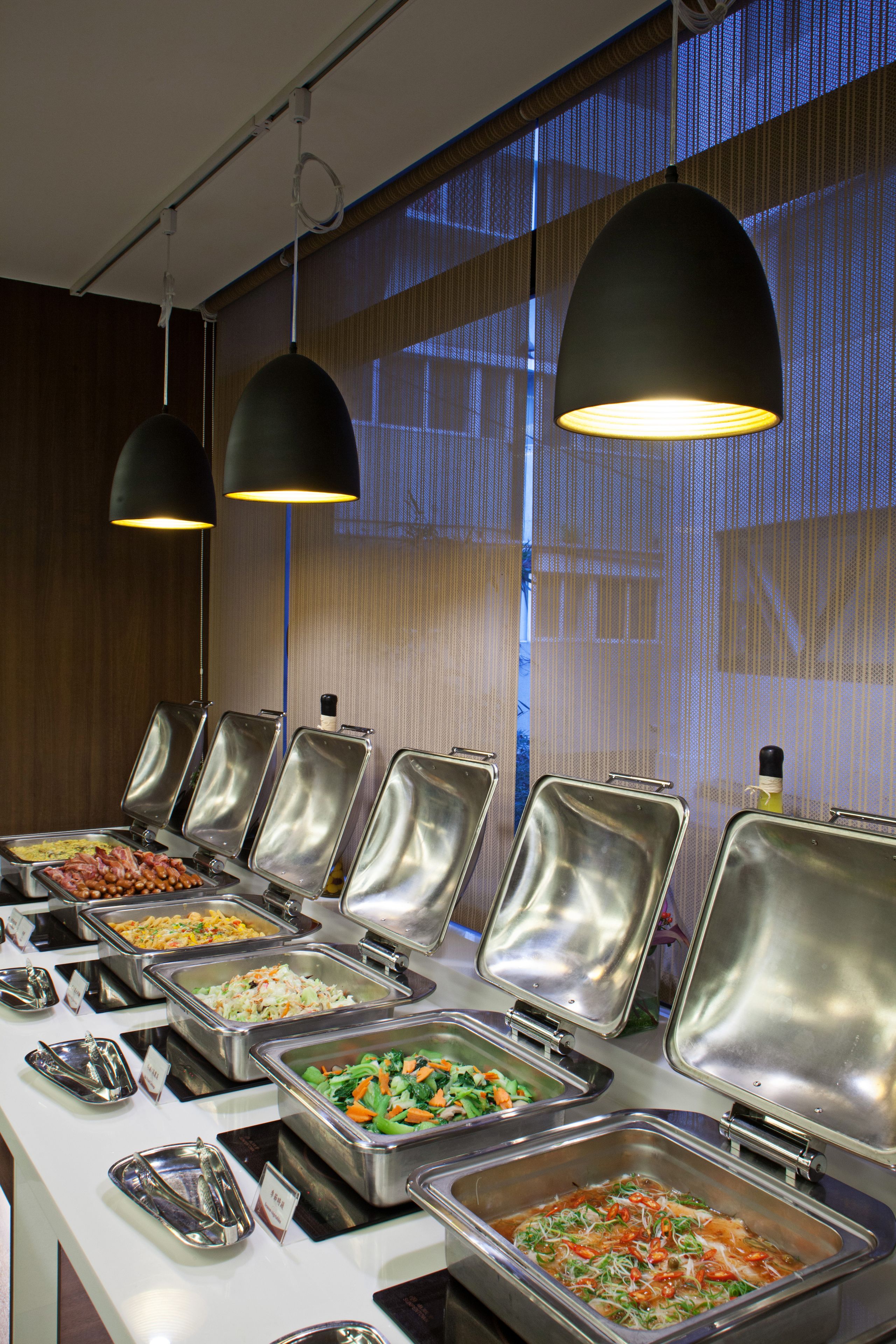 A buffet setup with multiple food stations, each with a metal serving tray and a lid.