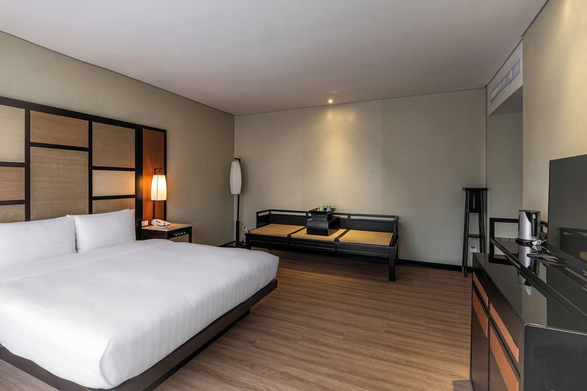 A hotel room with a large bed, a sofa, a desk with a chair, a TV, and a lamp.