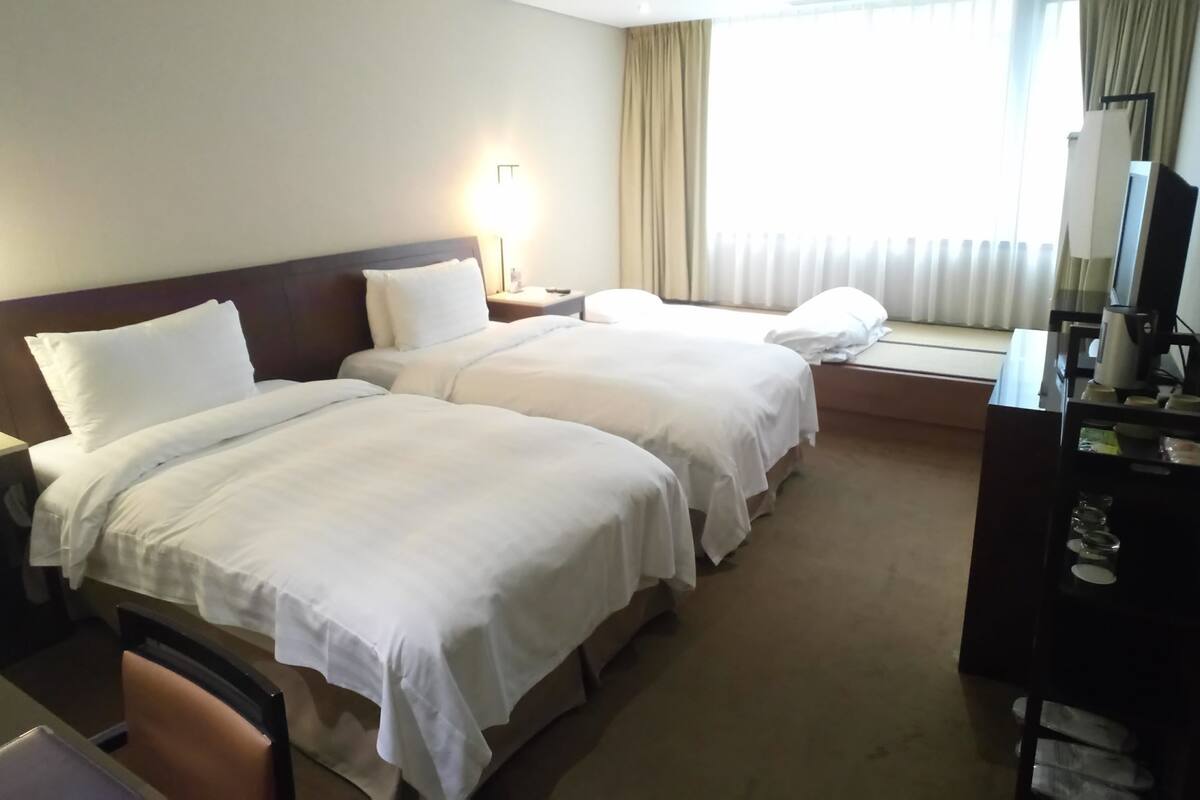 A hotel room with two beds, a desk, a chair, a TV, and a minibar.