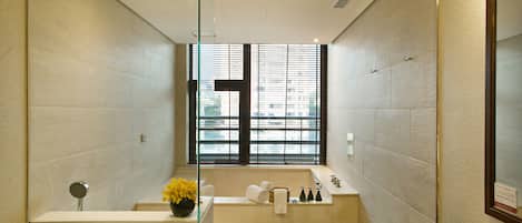 A modern bathroom with a bathtub, a shower, and a window with blinds.