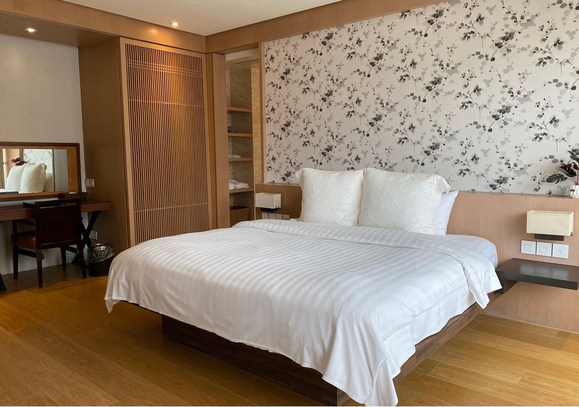 Una habitación de hotel moderna con una cama grande, un escritorio de madera, un armario y un papel tapiz floral.