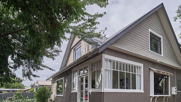A two-story house with a covered porch, large windows, and a sloped roof. - Racecourse Villa (Christchurch)