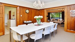 A dining area with a white table and chairs, a vase with flowers, and a clock on the wall. - Racecourse Villa (Christchurch)