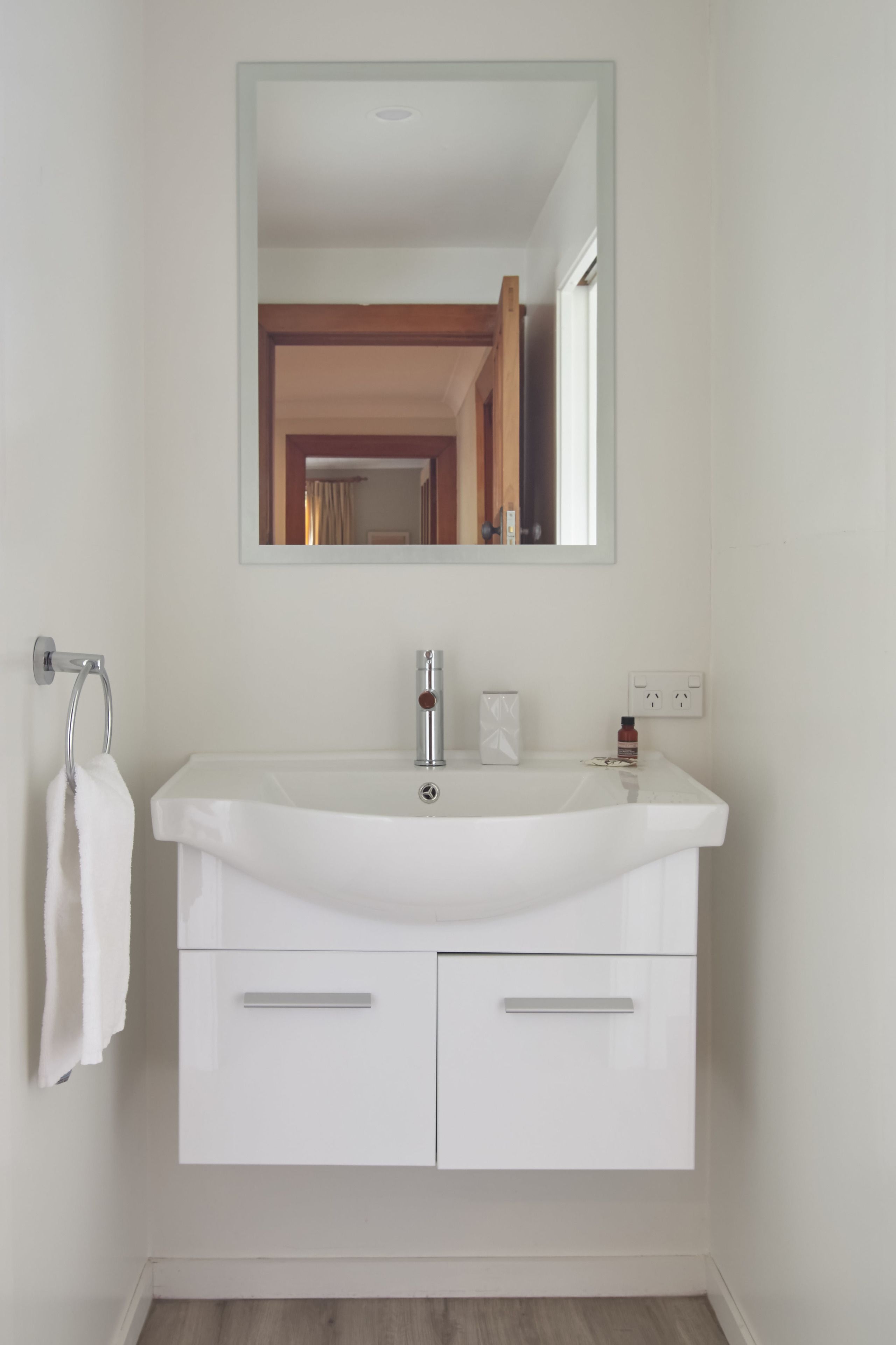 Un meuble-lavabo blanc pour la salle de bain, avec un miroir, un porte-serviettes et un lavabo.