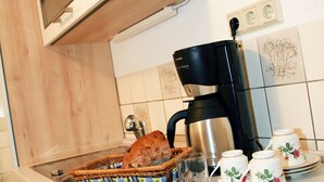 A kitchen with wooden cabinets, a coffee maker, a cutting board with fruits and cheese, and a sink. - "Bergblick" guest apartment near Löbauer Berg (Upper Lusatia) (Löbau)