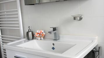 Ein modernes Badezimmer mit einem weißen Waschbecken, einem Edelstahlarmaturen und einem Spiegel darüber.