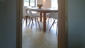 An open-plan dining area with a wooden table and white chairs, a large window with a view of greenery, and exposed wooden beams on the ceiling. - Old renovated farmhouse, ca.1840, high quality furnishings with Bodden view (Ummanz)