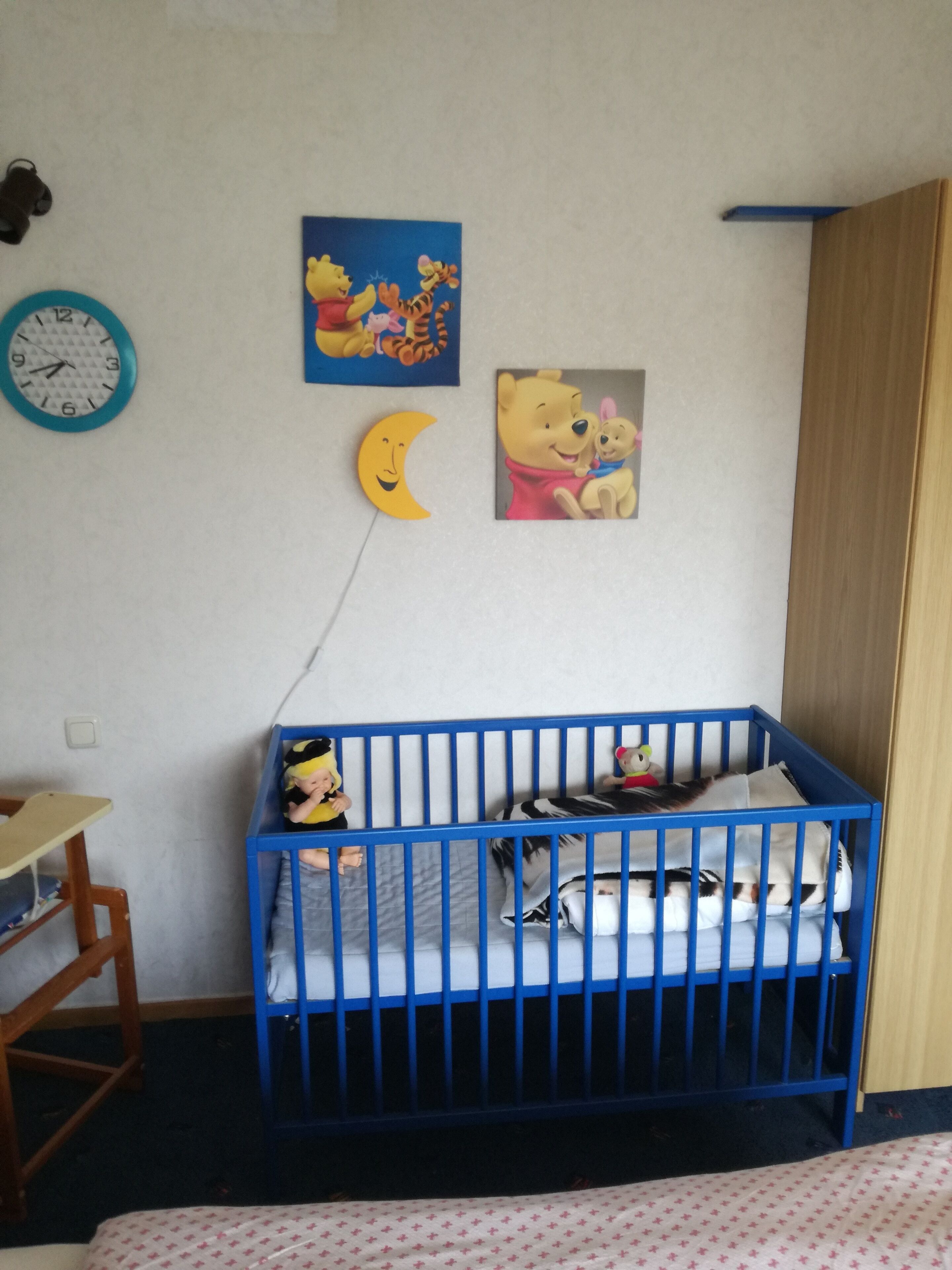 En rejse seng med legetøj, et ur og to Winnie the Pooh plakater på væggen.