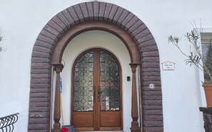Une entrée d’immeuble avec une porte en bois, une fenêtre en verre ornée de motifs métalliques et un arc en briques.