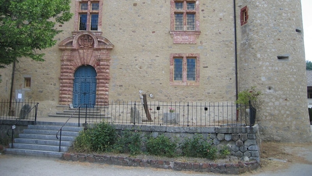 A stone building with a central entrance, a staircase leading up to it, and a metal fence in front.