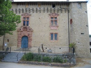Un bâtiment en pierre avec une entrée centrale, un escalier menant à cette entrée et une clôture en métal à l’avant.
