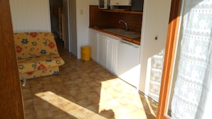 A compact kitchen with a microwave, sink, and cabinets. A yellow trash can is visible.