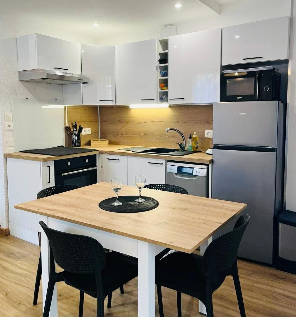 Een moderne keuken met witte kasten, een houten eettafel, zwarte stoelen, een ingebouwde oven, een vaatwasser en een magnetron.