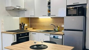 A modern kitchen with white cabinets, a wooden dining table, black chairs, a built-in oven, a dishwasher, and a microwave.